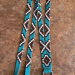 May include: A turquoise beaded lanyard with a brown and white geometric pattern and a silver swivel clasp.