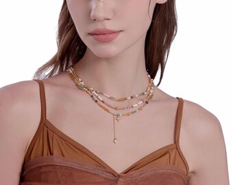 May include: A layered necklace with multiple strands of colourful beads and a pendant with a small pearl. The necklace is worn by a person wearing a brown top. The beads are of varying sizes and colours, creating a delicate and intricate design.