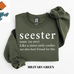 May include: A green sweatshirt with the word "seester" defined as "like a sister, only cooler." The text is in white and the sweatshirt is labeled "Military Green."