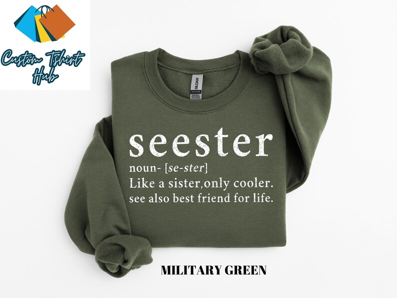 May include: A green sweatshirt with the word "seester" defined as "like a sister, only cooler." The text is in white and the sweatshirt is labeled "Military Green."