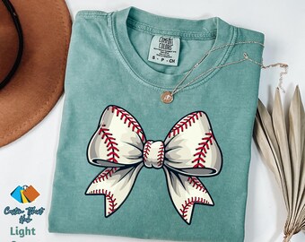 May include: A light green t-shirt with a white and red baseball-themed bow. The shirt has the text "COMFORT COLORS" and "S - P - CH" printed on the front.