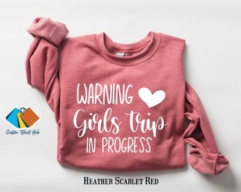 May include: A heather scarlet red sweatshirt with the text "WARNING Girls Trip IN PROGRESS" and a white heart.