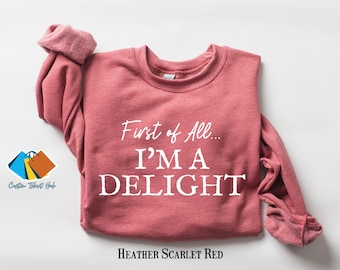 Könnte beinhalten: Ein langärmliger Sweatshirt in Heidelbeer-Scharlachrot mit dem Aufdruck "First of All... I'm a Delight" in Weiß.