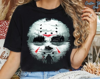 May include: Black t-shirt featuring a graphic design of a hockey mask with a lake scene, a boat, and a figure holding a weapon. The design includes red accents and the text "Custom T-shirt Hub".