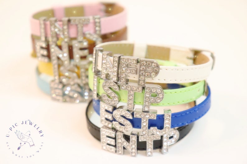 May include: Stack of colorful leather bracelets with a silver charm spelling out "INFP ESTJ ENTP".