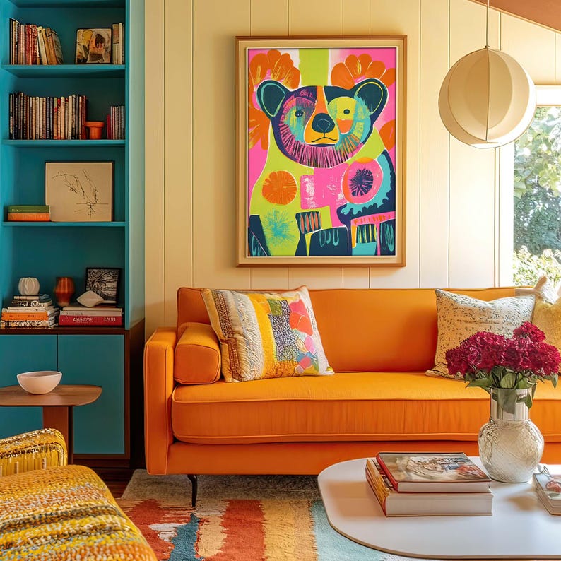 May include: A bright orange sofa with colorful patterned pillows sits in a living room with a large framed print of a colorful bear. The room has a teal blue bookshelf and a white ceiling lamp.