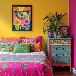 Op de afbeelding: Een kleurrijke slaapkamer met een felgele muur, een bed met een roze en veelkleurige bedsprei en een dressoir met bloemmotieven. Het dressoir heeft drie lades en is geschilderd in tinten blauw, groen en oranje. Er hangt een ingelijst afdruk van een kleurrijke beer aan de muur boven het bed.