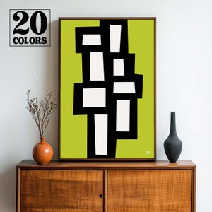 May include: Abstract geometric art print with black and white shapes on a lime green background. The print is framed and hanging on a wall above a wooden cabinet.