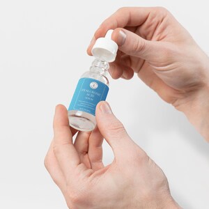 Puede incluir: Una botella de vidrio transparente con un gotero y una etiqueta azul que dice "HYALURONIC ACID SERUM".
