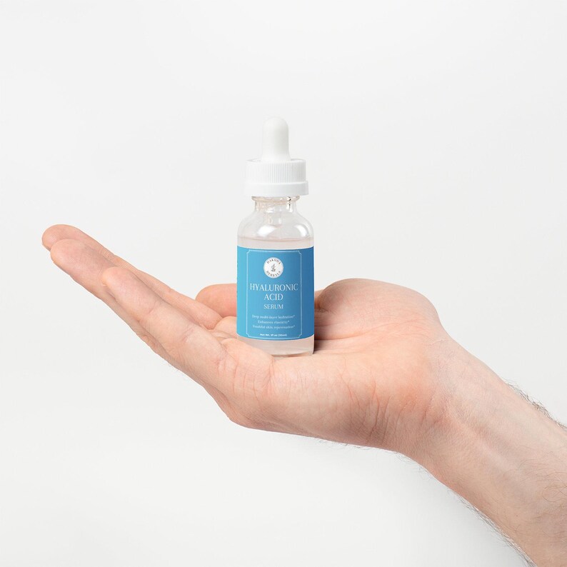 Puede incluir: Una botella de vidrio transparente con un gotero blanco y una etiqueta azul que dice "HYALURONIC ACID SERUM".