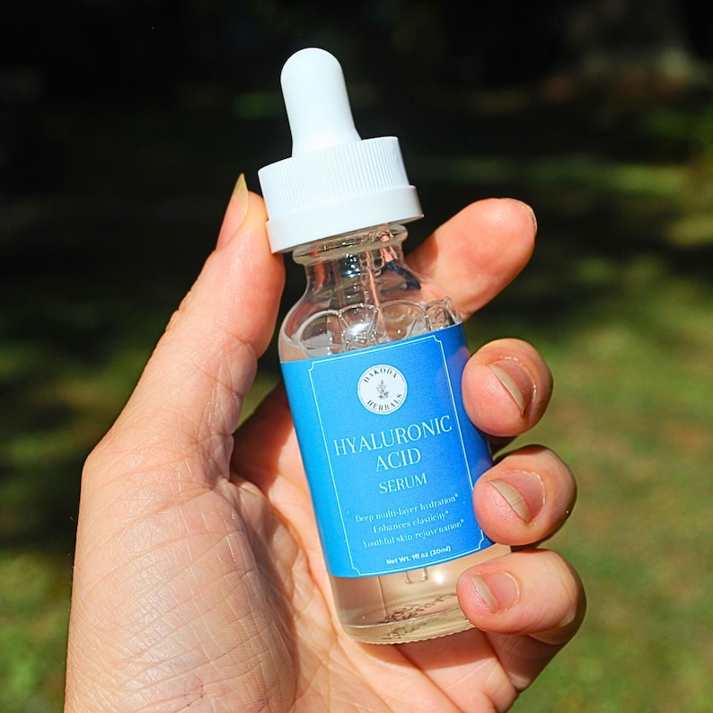 Puede incluir: Una botella de vidrio transparente con un gotero blanco y una etiqueta azul que dice "Hyaluronic Acid Serum" con el texto "Hidrata y humecta profundamente* Mejora la elasticidad de la piel* Rejuvenecimiento de la piel* Contenido neto: 30 ml (1 fl oz)"