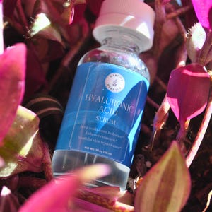 Puede incluir: Una botella de vidrio azul con tapa blanca que contiene suero de &aacute;cido hialur&oacute;nico. La botella est&aacute; etiquetada con el texto "DAKO HERBALS" y "HYALURONIC ACID SERUM". La etiqueta tambi&eacute;n incluye el texto "Hidrataci&oacute;n multicapa profunda", "Mejora la elasticidad", "Rejuvenecimiento de la piel", y "Peso neto 1 fl oz (30ml)".