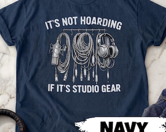 May include: A navy blue t-shirt featuring a white graphic of studio equipment including a microphone, coiled cables, and headphones hanging from a rack. The text reads, IT'S NOT HOARDING IF IT'S STUDIO GEAR, printed in a distressed white font.