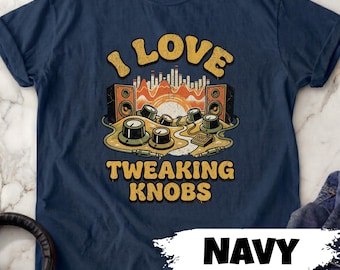 May include: Navy blue t-shirt with a retro graphic that says "I LOVE TWEAKING KNOBS". The design features speakers, knobs, and a sound wave illustration in shades of orange, yellow, and white. The word "NAVY" is also visible.
