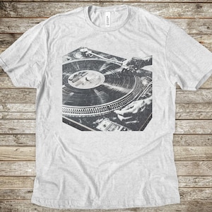 May include: A black and white photo of a hand mixing a record on a turntable. The turntable is a classic style with a black vinyl record on it.