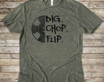 May include: A heathered olive green short-sleeve t-shirt featuring a black graphic of a half vinyl record on the left side and the text DIG. CHOP. FLIP. printed in a bold, distressed black font on the right side of the chest area.