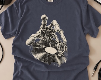 May include: A slate blue short-sleeve t-shirt featuring a graphic print of a skeletal hand reaching down to touch a black vinyl record on a turntable. The shirt has a crew neckline and a Comfort Colors brand label printed on the inside collar.