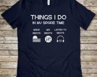 May include: A navy blue short-sleeve t-shirt featuring white text that reads THINGS I DO IN MY SPARE TIME, followed by three columns: MAKE BEATS with a piano icon, MIX BEATS with a sound mixer icon, and LISTEN TO BEATS with a headphone icon.