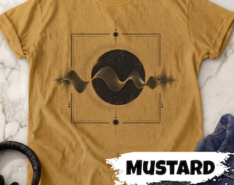 May include: Mustard-colored t-shirt featuring a black graphic design. The design includes a central black circle with a wavy line pattern, framed by a square and radiating lines. The word "MUSTARD" is written in white.