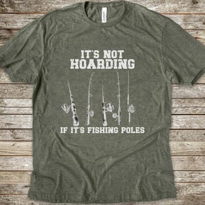 Op de afbeelding: Een olijfgroen gem&ecirc;leerd T-shirt met korte mouwen en een witte afbeelding van vijf hengels. De in het wit gedrukte tekst luidt: IT'S NOT HOARDING IF IT'S FISHING POLES. Het T-shirt heeft een ronde hals en een standaard pasvorm.