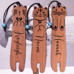 以下が含まれることがあります： 名前入りのかわいい猫のウッドブックマーク3個セット。Kayleigh、Naomi、Hannahの名前入り。各ブックマークには、青いビーズが付いたかわいい猫のデザインが施されています。