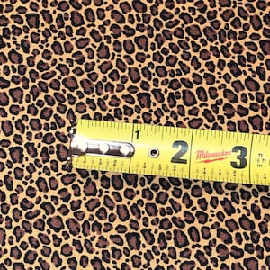 May include: Close-up of a yellow measuring tape with black markings, showing 2 inches. The tape is lying on a brown fabric with a leopard print pattern.