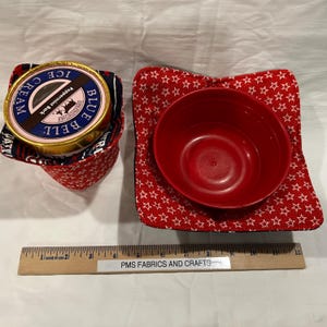 May include: Two red and white star-patterned fabric bowl cozies. One cozy is holding a red bowl, the other is holding a pint of Blue Bell Peppermint Bark ice cream.