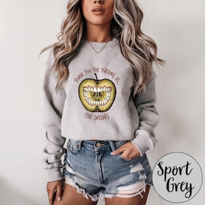 Könnte beinhalten: Sport Grey Sweatshirt mit einem Grafikdesign eines grünen Apfels mit Zähnen und dem Text "Thank You for Teaching Us The Insides". Das Sweatshirt hat einen Rundhalsausschnitt.
