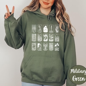Może przedstawiać: Zielona bluza z kapturem w kolorze wojskowym z białym wzorem kart tarota. Wz&oacute;r zawiera r&oacute;żne ilustracje kart tarota z tekstem. Bluza z kapturem ma kaptur ze sznurkiem i przednią kieszeń.