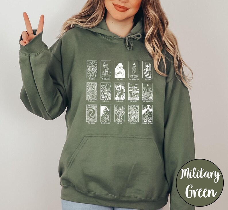 Może przedstawiać: Zielona bluza z kapturem w kolorze wojskowym z białym wzorem kart tarota. Wz&oacute;r zawiera r&oacute;żne ilustracje kart tarota z tekstem. Bluza z kapturem ma kaptur ze sznurkiem i przednią kieszeń.