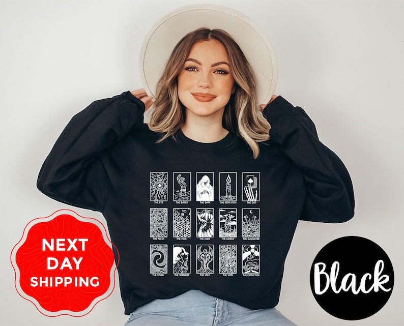 Może przedstawiać: Czarna bluza z białym wzorem kart tarota. Wz&oacute;r zawiera r&oacute;żne ilustracje kart tarota z tekstem. Bluza jest w jednolitym czarnym kolorze.