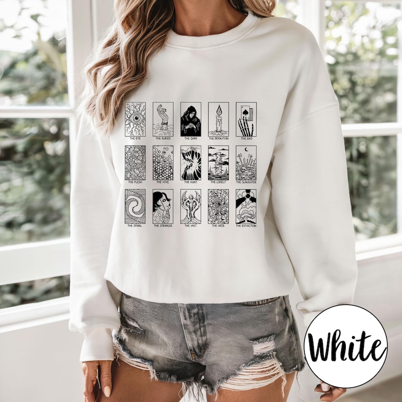 Może przedstawiać: Biała bluza z czarnym nadrukiem kart tarota. Grafika zawiera r&oacute;żne symbole i tekst, ze słowem "White" w okręgu po prawej stronie. Bluza to casualowy element garderoby z długimi rękawami.