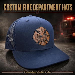 May include: A navy blue trucker hat featuring a brown leather patch on the front. The patch is shaped like a Maltese cross and displays a fire truck, a ladder, a tree, and the text OAK ISLAND FIRE DEPT. The hat has a mesh back panel.