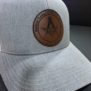 May include: Gray baseball cap with a brown leather patch. The patch features the words "Balfour Lodge #188 A.F. & A.M." and "EST. 1855" surrounding a compass and square symbol. The cap has a curved brim and white stitching.