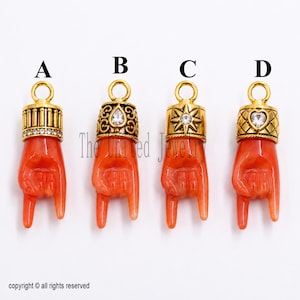 May include: Four coral-colored hand-shaped pendants labeled A, B, C, and D. Each pendant features a gold-tone metal cap with a jump ring. The caps are decorated with clear rhinestones in various shapes including a star and a heart.