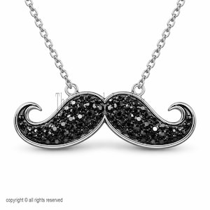 May include: A silver-toned necklace featuring a mustache pendant encrusted with black crystals. The mustache design has curved ends and is suspended from a delicate chain. The image is set against a white background.