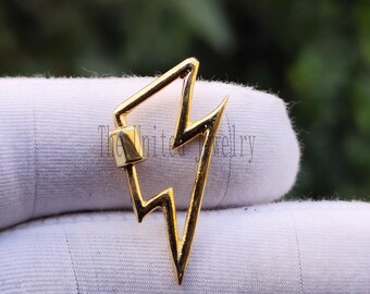 May include: A gold-colored lightning bolt-shaped clasp. The clasp has a rectangular top section and a pointed bottom, with a zig-zag design in the middle. The clasp is shown against a white background.