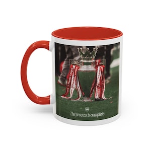 May include: White ceramic mug with a red interior and handle. The mug features an image of a trophy with red ribbons and the text "Premier League." The words "The process is complete" are printed on the mug.