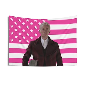 Puede incluir: Un tapiz rectangular con una persona con abrigo burdeos y camisa blanca frente a una bandera estadounidense rosa y blanca. La persona sostiene un libro gris. Ideal para decoración de pared.