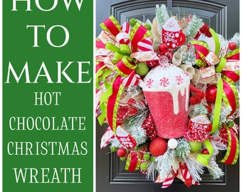 May include: A red and green Christmas wreath with a hot chocolate mug decoration. The wreath is decorated with red and white striped ribbon, green and white ribbon, and a brown burlap bow. The wreath also has a small gingerbread man ornament and a white ornament with the text "Let it snow".