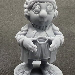 May include: A gray 3D printed figurine of a small humanoid character with curly hair, wearing a buttoned jacket and trousers, standing on a circular base. The character has large eyes, a rounded nose, and bare feet with visible toes.