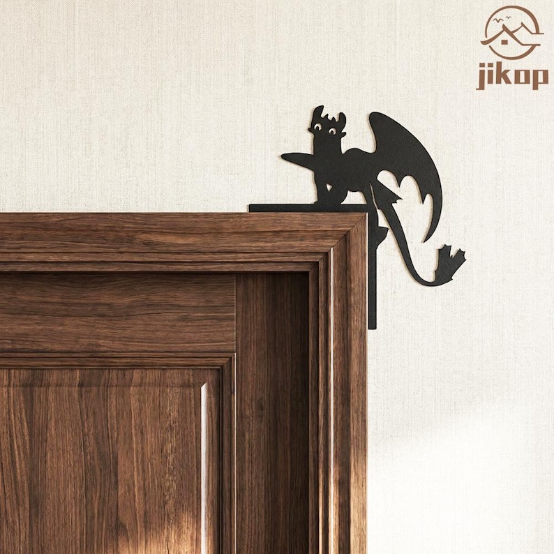 May include: Black metal dragon corner decor. The dragon is a silhouette with outstretched wings and a long tail. It is mounted on the corner of a wooden door frame. The dragon is a decorative accent piece.