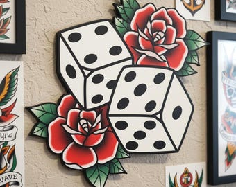 Pode incluir: Decoração de parede com dois dados brancos com pontos pretos, sobre rosas vermelhas e folhas verdes. Os dados e as rosas são em estilo de tatuagem tradicional, com contorno preto. Outras artes de tatuagem emolduradas são visíveis.