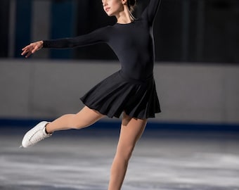 May include: A black long-sleeved figure skating dress with a fitted bodice and a short, flared skirt. The garment is worn with white lace-up ice skates featuring metal blades, designed for performance on an ice rink surface during skating.