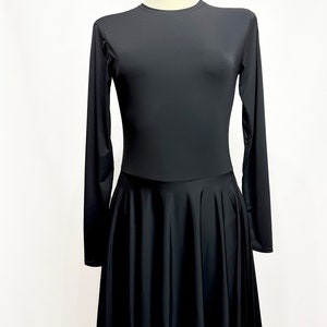 Può includere: Abito nero a maniche lunghe con scollo tondo e gonna svasata. L'abito è esposto su un manichino su sfondo bianco. Il tessuto sembra essere di colore liscio e uniforme.