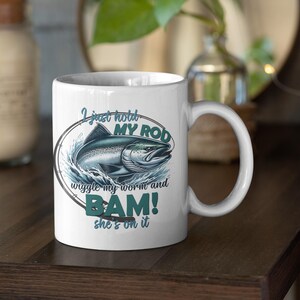 May include: White ceramic coffee mug with a blue and green illustration of a fish and the text "I just hold my rod wiggle my worm and BAM! she's on it"