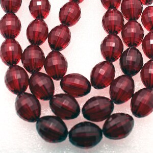 May include: A strand of deep red faceted glass beads. The beads are oval shaped and have a smooth, polished finish.