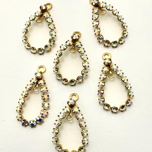 May include: Six teardrop-shaped jewelry charms. Each charm features a gold-toned metal frame encrusted with iridescent, multi-colored rhinestones. The charms have a small loop at the top for attaching to jewelry.