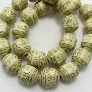 May include: A strand of cream-colored beads with gold-colored etched designs. The beads are round and have a slightly textured surface.