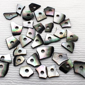 May include: A collection of black and iridescent shell beads with a hole in the center of each bead. The beads are irregularly shaped and have a natural, organic look.